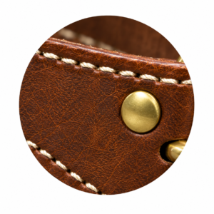 Close-up of premium cream-colored stitching on rich brown leather, showcasing detailed threadwork, textured leather grain, reinforced seams, and a brass rivet. High-quality craftsmanship by John Leatherwear.